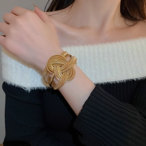 Close-up of a wide gold metal layered cuff bracelet with an intricate woven knot design