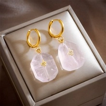 Close-up of pink faceted drop earrings featuring a golden snake motif inside a jewelry box