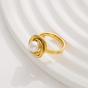 Macro shot of gold spiral ring with centered white pearl on wavy white surface