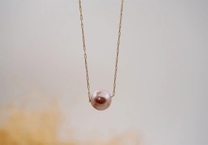 Macro detail of a single round pink pearl pendant on a delicate gold chain necklace