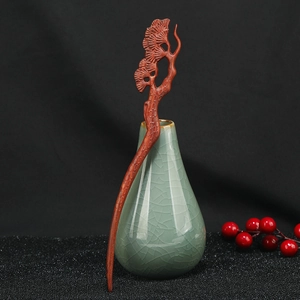 Detailed view of hand-carved sandalwood hair stick with pine branch motif in red-brown finish