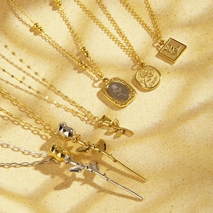 Vintage gold rose pendant necklaces set with floral embossed round coins on sandy background