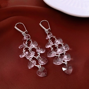 Detailed shot of silver tassel earrings with pink heart-shaped crystal beads on red silk