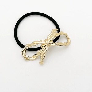 Detail view of a black elastic hair tie with a textured gold-tone alloy bow decoration