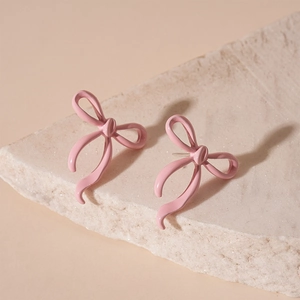 Close-up of small pink lacquer bow stud earrings on a natural stone background