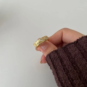 Detailed view of wide gold irregular textured ring featuring three white cubic zirconia stones