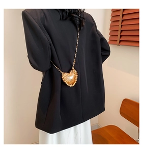 Detail of a golden heart-shaped mini crossbody bag with sunburst texture and chain strap