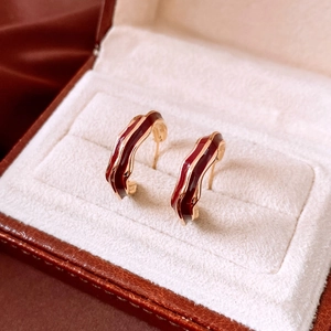 Macro detail of wavy C-shape earrings with burgundy enamel and gold plating finish