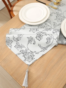 Close-up of silver-grey jacquard table runner with black floral pattern and tassel