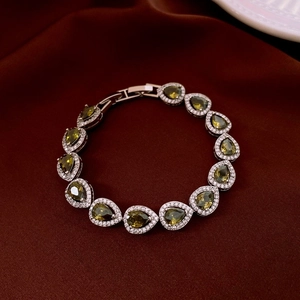 Gros plan de pierres ovales vert olive et zircons sur un bracelet argenté sur satin rouge