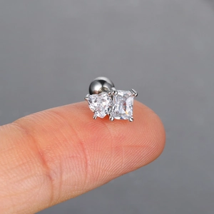 Close-up of a tiny silver piercing stud with heart and square zircon on a fingertip
