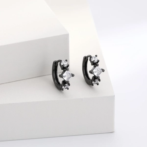 Macro detail of black square zircon huggie earrings on a minimalist white geometric stand