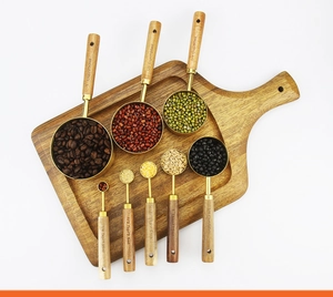 Flat lay of 8-piece gold measuring cups and spoons with wood handles and grains