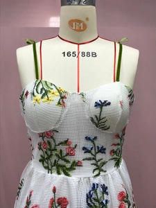 Detail von Blumenstickerei auf weißem Netzkleid mit grünen Samträgern und schmaler Taille