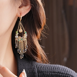 Detailed view of gold tassel earrings with emerald and zircon stones on a model