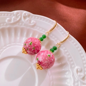 Dettaglio di orecchini vintage con perle di vetro floreali rosa su un piatto di ceramica
