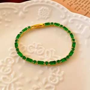 Vintage 18K gold plated tennis bracelet with emerald cut green stones on porcelain