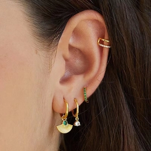 Close-up of gold fan-shaped earrings with green zircon gems on a model's ear