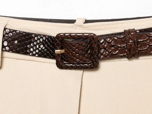 Détail d'une ceinture marron foncé aspect serpent avec boucle carrée sur pantalon beige