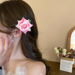 Detailed close-up of a pink fabric rose hair clip with green leaves on wavy brown hair