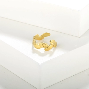 Detailed view of a gold-plated metal open ring featuring embossed face pattern on white block
