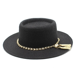 Détail du chapeau de paille noir avec chaîne dorée, perles et pompons blancs décoratifs