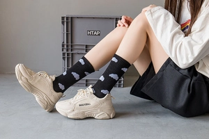 Detail of black mid-calf socks with blue cloud patterns worn with chunky beige sneakers