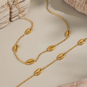 Macro shot of gold shell necklace charms on light beige surface with driftwood decor
