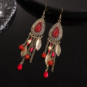 Close-up of vintage bronze earrings with red beads, metal leaves and long tassels