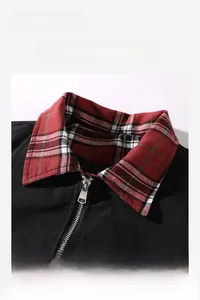 Detail of black jacket featuring a red and green plaid collar and silver metal zipper