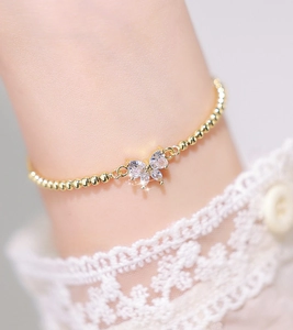Detail of a sparkling zircon butterfly charm on a delicate golden beaded pull bracelet