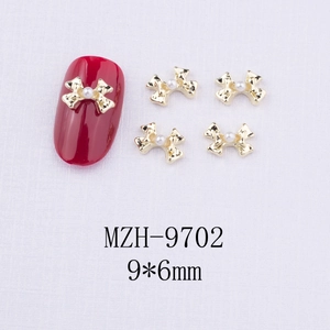 Vue macro de bijoux d'ongles nœuds dorés 9x6mm avec perles sur fond violet texturé