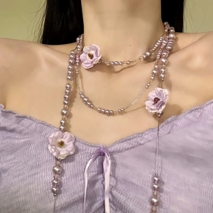 Macro close-up view of a sweet purple pearl necklace with fabric flowers on model.