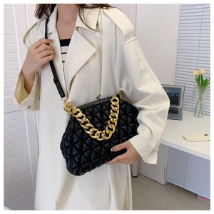 Fashionable model wearing a black quilted crossbody bag with a thick gold chain strap