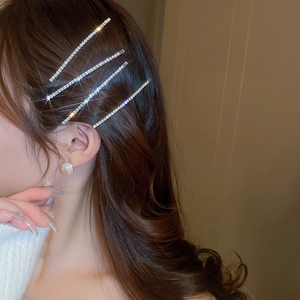 Detailed view of four sparkling rhinestone bobby pins styled on wavy brown hair
