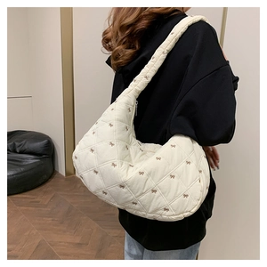 Makrodetail der beigen Stepptasche mit eleganter brauner Schleifenstickerei