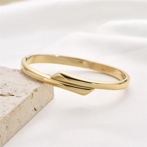Polished gold geometric stainless steel hollow bangle displayed on a natural stone base