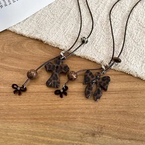 Collier croix léopard et nœud avec perles en résine sur fond tissé rustique