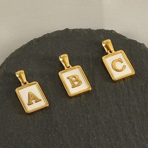 Macro view of gold rectangular alphabet pendants with white enamel inlay on a stone surface