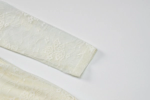 Detaillierte Nahaufnahme von feinem Spitzenstoff und Ärmelbündchen am cremefarbenen Kleid
