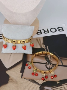Detailed macro of gold-plated strawberry and cherry charms on modular link bracelets
