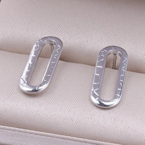Macro detail of oval stainless steel stud earrings with textured horizontal carvings
