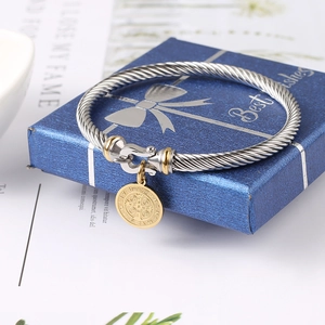 Close-up of twisted stainless steel cable bracelet with gold Saint Benedict pendant