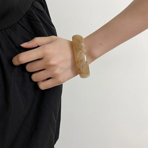 Close-up of a wide amber resin bangle featuring unique marble texture on a model's wrist