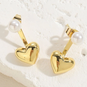 Makro-Detail von 14K Gold-Herzohrringen mit weißen Perlen auf einer Steinoberfläche