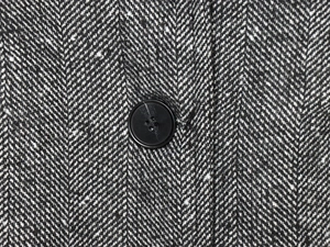Macro shot of herringbone tweed fabric texture and black button on woman blazer
