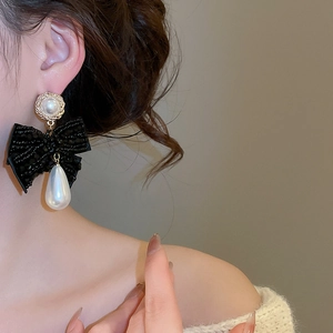 Close-up of elegant bow earrings with white teardrop pearls and black beads on a model