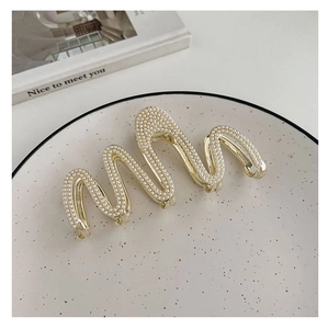 Detail view of a golden wave hair claw clip featuring elegant pearls on a white plate