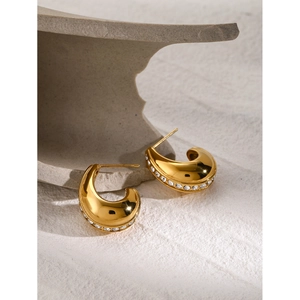 Detail view of 18k gold plated C-shaped earrings with white rhinestones on stone background