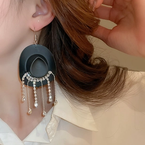 Macro view of black cowboy hat earrings with long silver rhinestone tassels on model